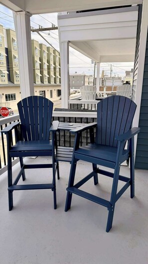Ein überdachter Außenbereich mit zwei Adirondack-Stühlen und einem Tisch, mit Blick auf eine Wohnstraße.