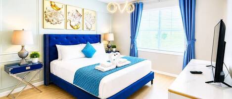 A hotel room with a large bed, a desk, a television, and artwork on the wall.