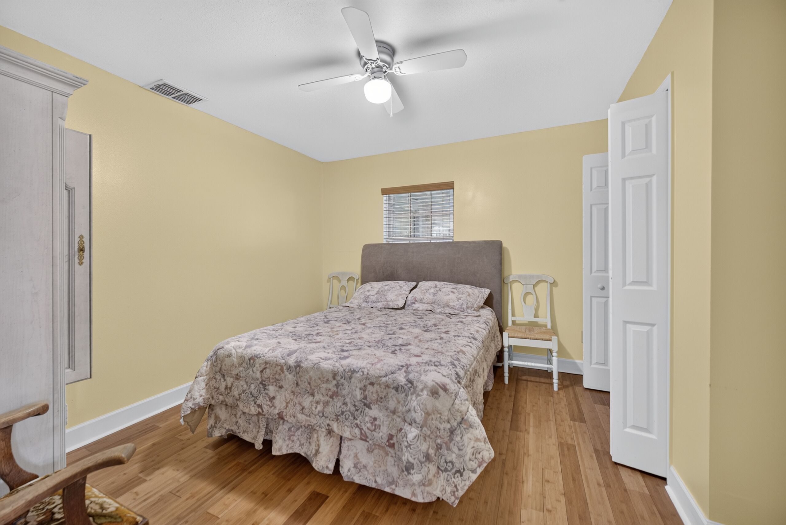 Quarto com cama, ventilador de teto, janela com persianas e uma porta.