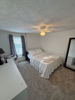Ein Schlafzimmer mit einem Bett, einem Schreibtisch, einem Globus, einem Deckenventilator und einem Fenster mit Vorhängen.