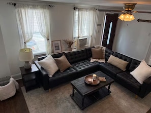 Ein Wohnzimmer mit schwarzem Ledersofa, einem Couchtisch, einer Lampe und einem Deckenventilator.