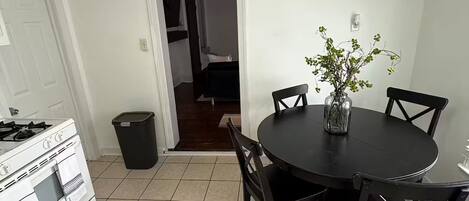 A kitchen with a stove, a dining table with chairs, and a trash can.