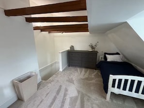 Ein Schlafzimmer mit schrägem Dach, einem Bett, einer Kommode und einer kleinen Pflanze.