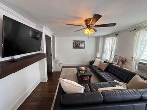 A living room with a large flat-screen TV, a black leather sofa, a ceiling fan, and a framed picture on the wall. - Fishtown home (Philadelphia)