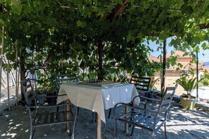 Un espace de restauration en plein air avec une table et des chaises, installé sous une pergola recouverte de vignes.