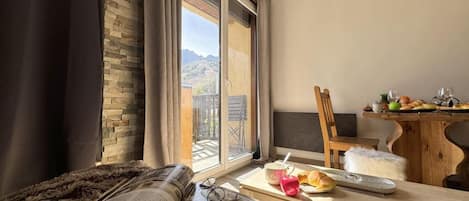 A cozy room with a large window, a dining table with breakfast items, a fluffy rug, and a book.