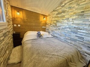 A narrow room with a bed, a plush rug, a teddy bear, and a stone wall. - 4th floor, balcony, ski locker, 26m², Vars (Vars)