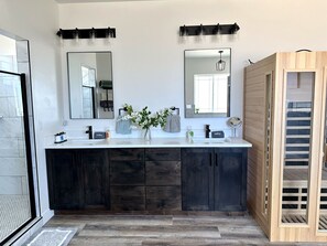 Un baño con tocador doble, armarios de madera oscura, un espejo grande y una puerta de madera.