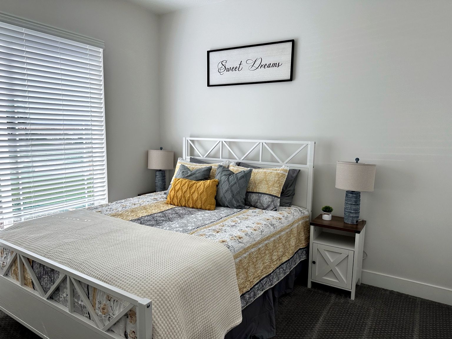 A bedroom with a bed, bedside lamps, a wall-mounted picture frame, and a window with blinds.