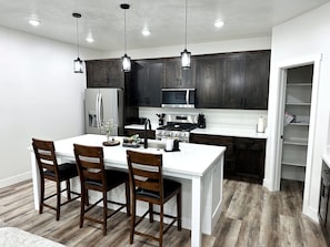 Una cocina moderna con armarios de madera oscura, una isla blanca con taburetes de bar, electrodomésticos de acero inoxidable e iluminación colgante.