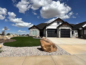 A modern two-story house with a stone facade, a well-maintained lawn, and a large rock feature in the foreground.