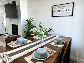 A dining area with a wooden table set for four, surrounded by potted plants and a welcome sign.