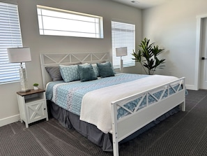 A bedroom with a bed, bedside tables, a potted plant, and windows.