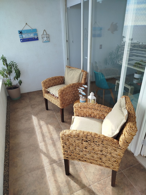 A balcony with wicker furniture, a potted plant, and a welcome sign.