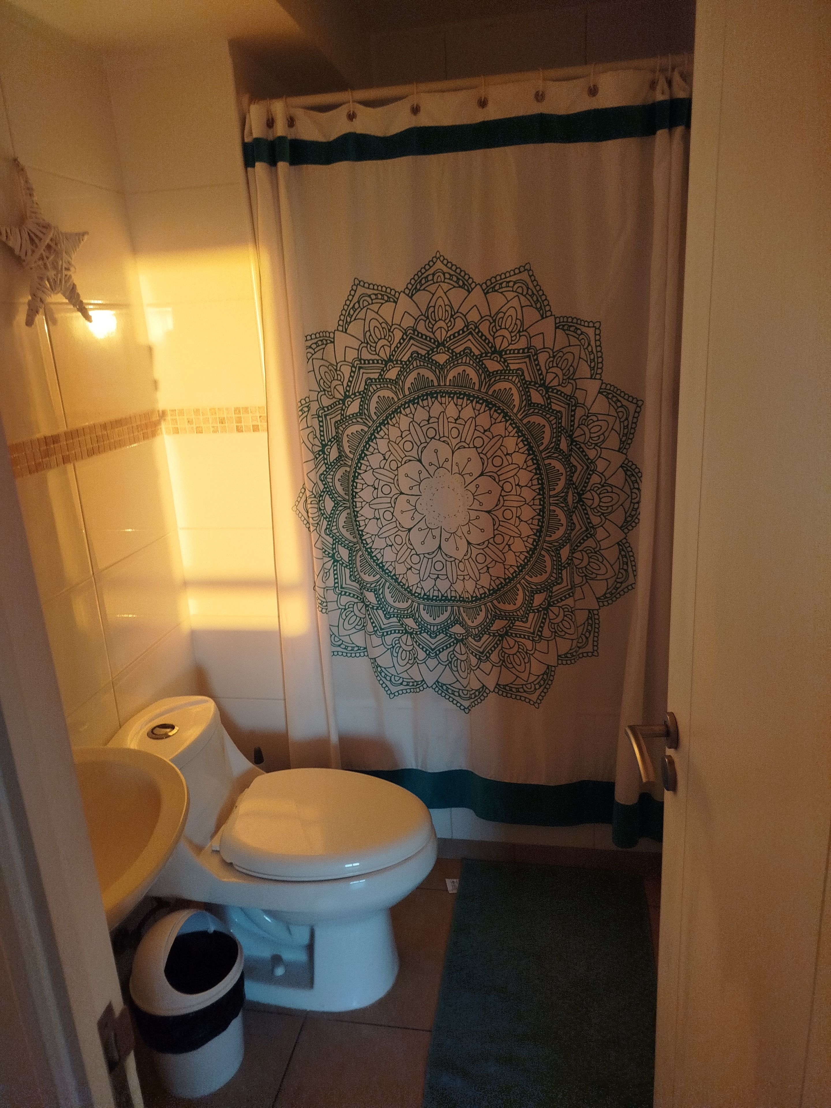 Een badkamer met toilet, wastafel en een douchegordijn met een mandala ontwerp.