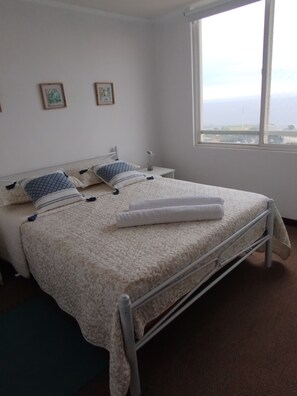 A single-bed room with a metal frame, a window with a view, and two framed pictures on the wall.