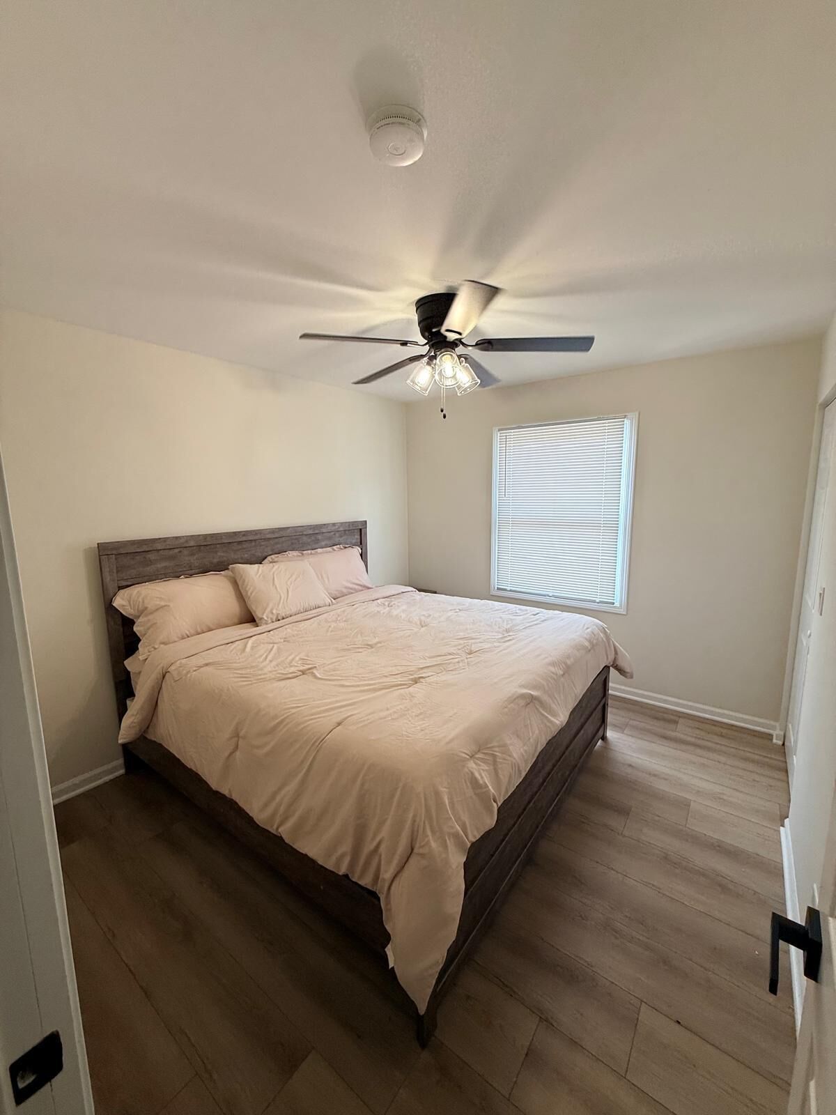 A bedroom with a bed, a ceiling fan, a window with blinds, and wooden flooring.
