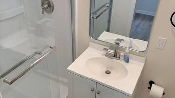 A bathroom with a glass shower enclosure, a white sink with a mirror above it, and a toilet.