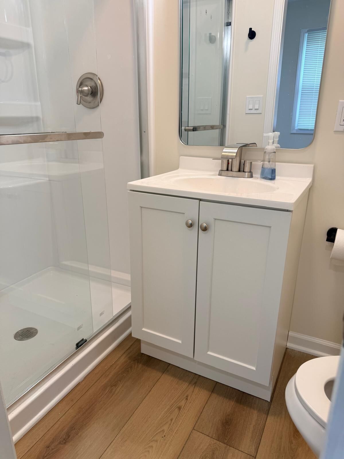 Un baño con cabina de ducha de vidrio, un lavabo blanco con espejo y un inodoro.