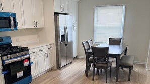 Une cuisine avec des meubles blancs, un réfrigérateur en acier inoxydable, une cuisinière et une table à manger avec des chaises.