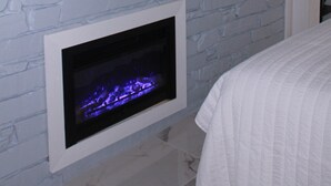 Ett rum med en öppen spis, en väggmonterad tv och en vit säng.