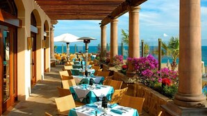 Ein Essbereich im Freien mit Tischen und Stühlen, einer Pergola und Blick auf den Ozean.