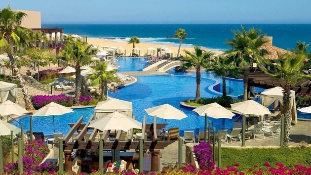Ein Resort mit Schwimmbad, Blick auf den Strand, Palmen und Liegestühlen.
