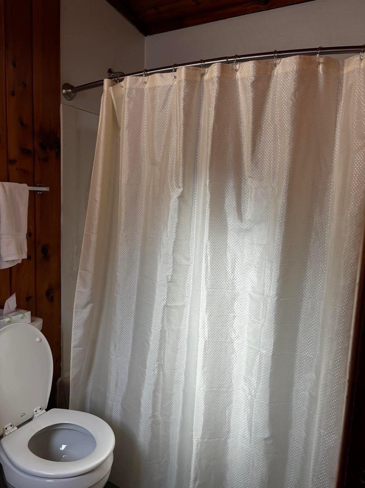 Une salle de bain avec des toilettes, un rideau de douche et un mur en bois.