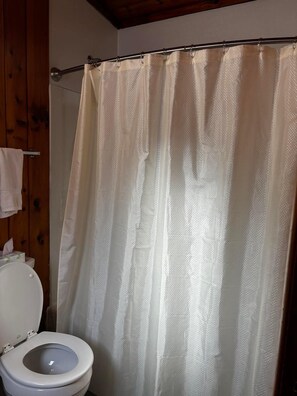 A bathroom with a toilet, a shower curtain, and a wooden wall. - Cozy 1BR hotel room, Hamilton - 320 Shenandoah (Hamilton)