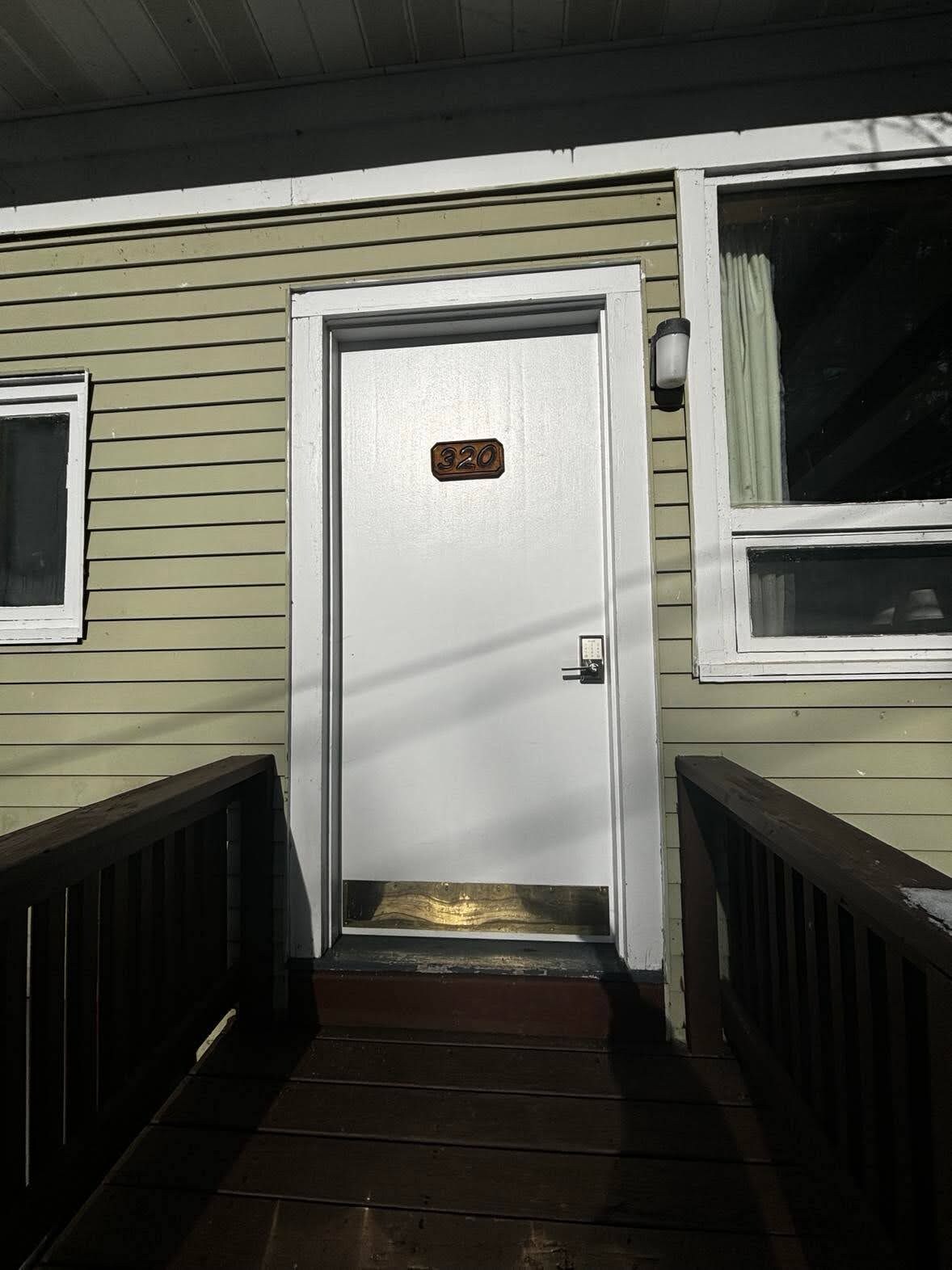 A front door with a number plate, a small window to the left, and a wooden staircase leading up to it.