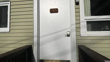 A front door with a number plate, a small window to the left, and a wooden staircase leading up to it.