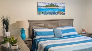 A bedroom with a bed, bedside tables, a lamp, a painting, and a plant. - Secrets Under the Palms - Luxury 1BR King Condo, Pond View Lanai (Lutz)