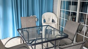 A glass-top table with four chairs, a white chair, and a blue curtain. - Secrets Under the Palms - Luxury 1BR King Condo, Pond View Lanai (Lutz)