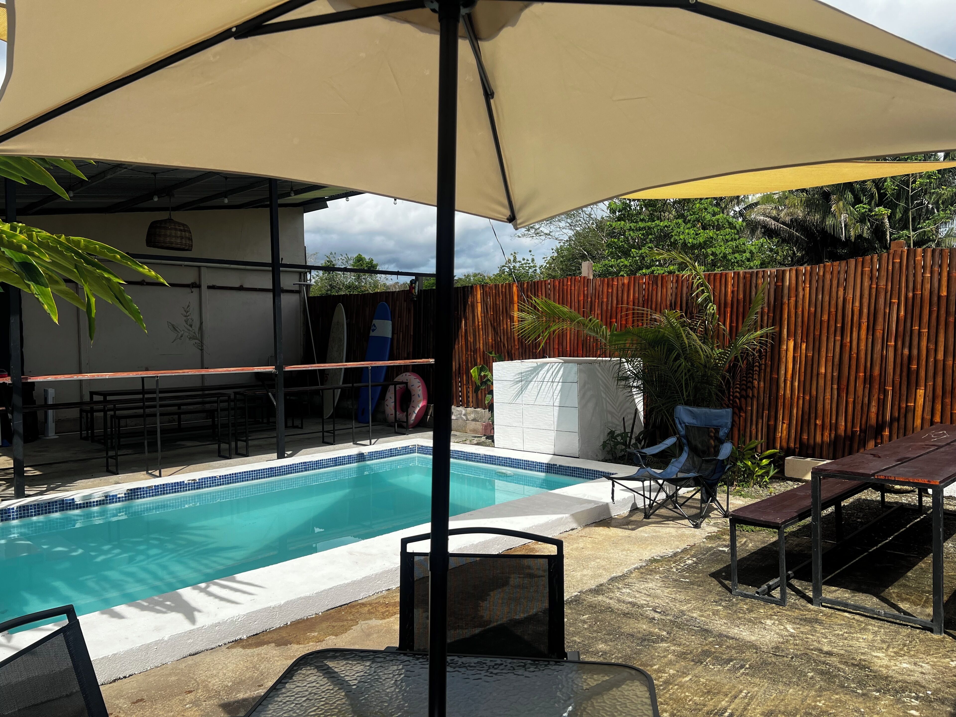 Uma piscina com área de estar coberta, cerca de madeira e móveis de exterior.