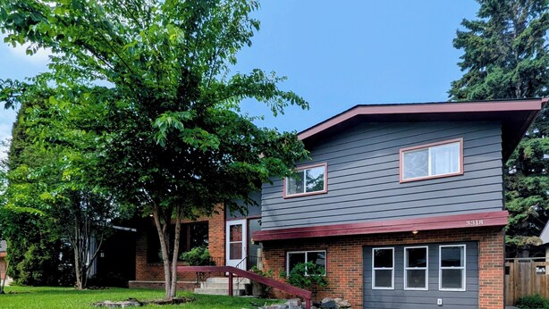 A two-story house with a stone retaining wall, a front yard, and a clear blue sky.