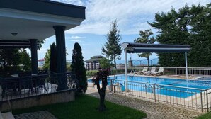 Una piscina con zona techada, pérgola y sendero de piedra.