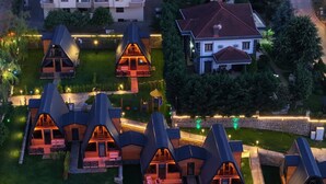 Un conjunto de cabañas modernas con techos triangulares y zonas de estar al aire libre, rodeadas de un césped cuidado y un muro de piedra.