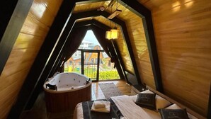 Un dormitorio acogedor en el ático, con techo inclinado de madera, un ventanal grande, una bañera de madera y una cama bien hecha.