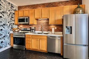 A kitchen with wooden cabinets, stainless steel appliances, a brick backsplash, and a black marble floor. - Downtown Walk To Restaurants Ferry By Cedar Point (Sandusky)