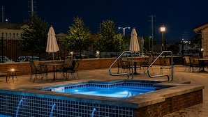 Una piscina con borde de azulejos, un área de descanso con sillas y sombrillas, y un muro de ladrillo.