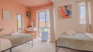 Quarto com duas camas, uma janela, escrivaninha e planta pendente.