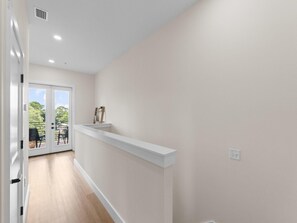 A hallway with a white wall, a wooden floor, and a door leading to an outdoor area with chairs and a table. - 3000 Blue Lagoon C (Panama City Beach)