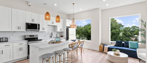 A modern kitchen with white cabinets, a central island, and bar stools. There is a dining area with a blue sofa and a round coffee table.