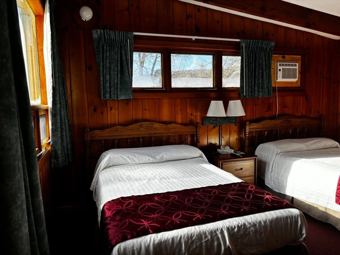 Une chambre avec deux lits, une table de chevet avec une lampe, une fenêtre avec des rideaux et un appareil de climatisation.