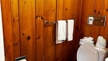 A wooden bathroom with a toilet, a towel rack with towels, and a toilet paper holder.