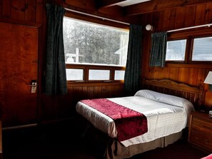 A wooden cabin bedroom with a bed, a nightstand, and a window with curtains. - Cozy 1BR hotel room, Hamilton - 321 Shenandoah (Hamilton)