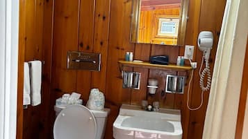 Un baño con paneles de madera, un inodoro, un lavabo y un secador de pelo.