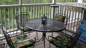 A covered outdoor area with a table and chairs, a sign reading 'Paris Cafe,' and a view of a forested area. - Paradise Point 3 BR home overlooking the bay in gorgeous Saint George Island (Saint George Island)