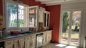 A kitchen with a dishwasher, a red wall, and a view of the garden through the door. - Family villa with a stunning view of the countryside, close to the beaches and marshes (Breuillet)