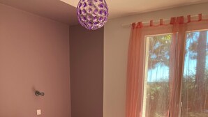 A bedroom with a wooden bed, a bedside table, a hanging light fixture, and a view through a window with sheer curtains. - Family villa with a stunning view of the countryside, close to the beaches and marshes (Breuillet)